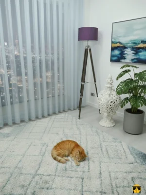 Modern bir oturma odası penceresinde, tavandan yere kadar uzanan, soft açık mavi tonunda, düz dökümlü, ferah ve dingin bir atmosfer yaratan şık tül perde