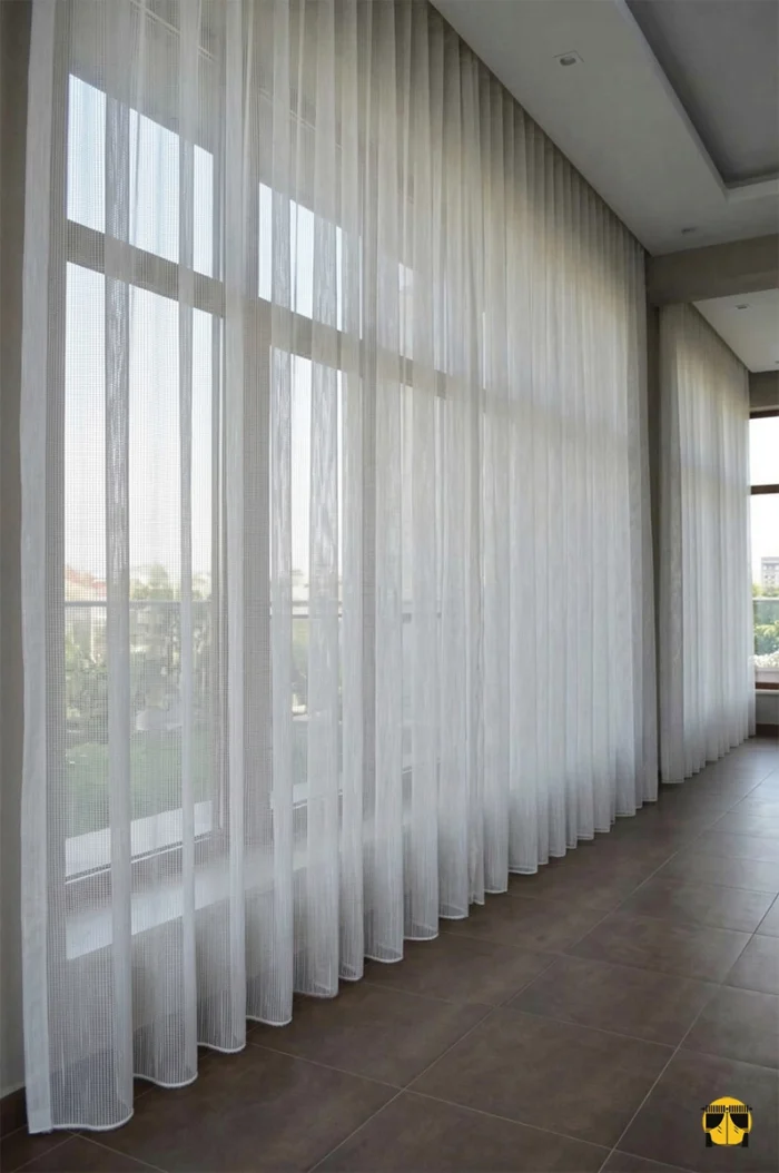 Modern bir salonda tavandan zemine kadar uzanan, odayı daha yüksek ve ferah gösteren çizgili kırık beyaz tül perde tasarımı