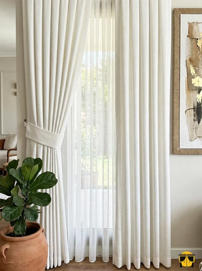 "Vizon mobilyalar ve ahşap detaylarla dekore edilmiş modern bir salonda, pencerelere zarafet katan açık krem fon perde tasarımı."