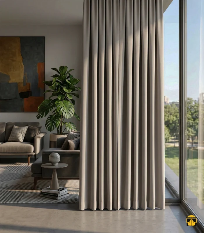 Modern bir oturma odasında, ön yüzü sakin gri tonunda, kenar kıvrımlarından ise vişne kırmızısı astarı gözüken, gün ışığını %100 bloke eden çift taraflı (duble) blackout fon perde.