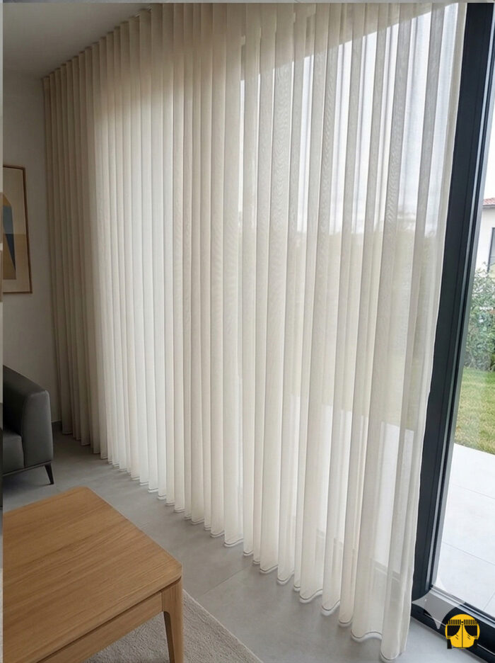 Kontrast ve Stil: "Siyah fon perdelerle kombinlenmiş, ağır dökümü sayesinde birer mimari sütun gibi muntazam inen açık gri düz krep tül perde sergisi."