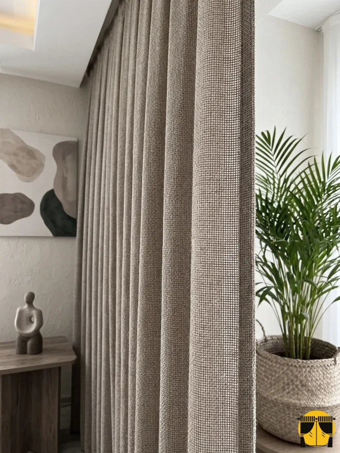 Kontrast ve Stil: "Ekru tül perdelerle kombinlenmiş, ağır dökümü sayesinde birer mimari sütun gibi muntazam inen sütlü kahve Boemo fon perde sergisi."