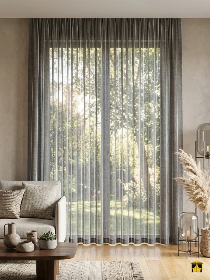 Modern bir salonda, dikine çizgili deseniyle tavanı daha yüksek gösteren ve gün ışığını dumanlı bir griyle süzerek içeri alan Tendo keten tül perde.