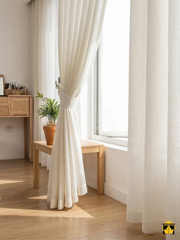 Güneş ışığını karemsi hasır dokusuyla süzerek odaya yumuşak bir aydınlık veren, halat kordonla şık bir şekilde bağlanmış Elton krem keten fon perde