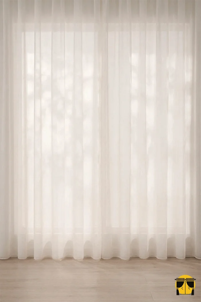 Beyaz duvarlar önünde zarif bir renk katmanı oluşturan, sık pileleri sayesinde sütun gibi muntazam inen dökümlü Pella pudra tül perde sergisi