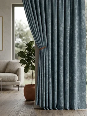 "Kabartma (embossed) dokuma teknolojisiyle üretilmiş mavi tonundaki dökümlü fon perde kumaşını ve deri bağlama aparatıyla şık duruşunu sergileyen yakın plan."