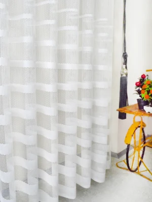 Muntazam dökümü sayesinde rüzgarda formunu bozmayan, ütü gerektirmeyen ve modern bir sportiflik sunan beyaz şeritli mutfak tül perde detayı
