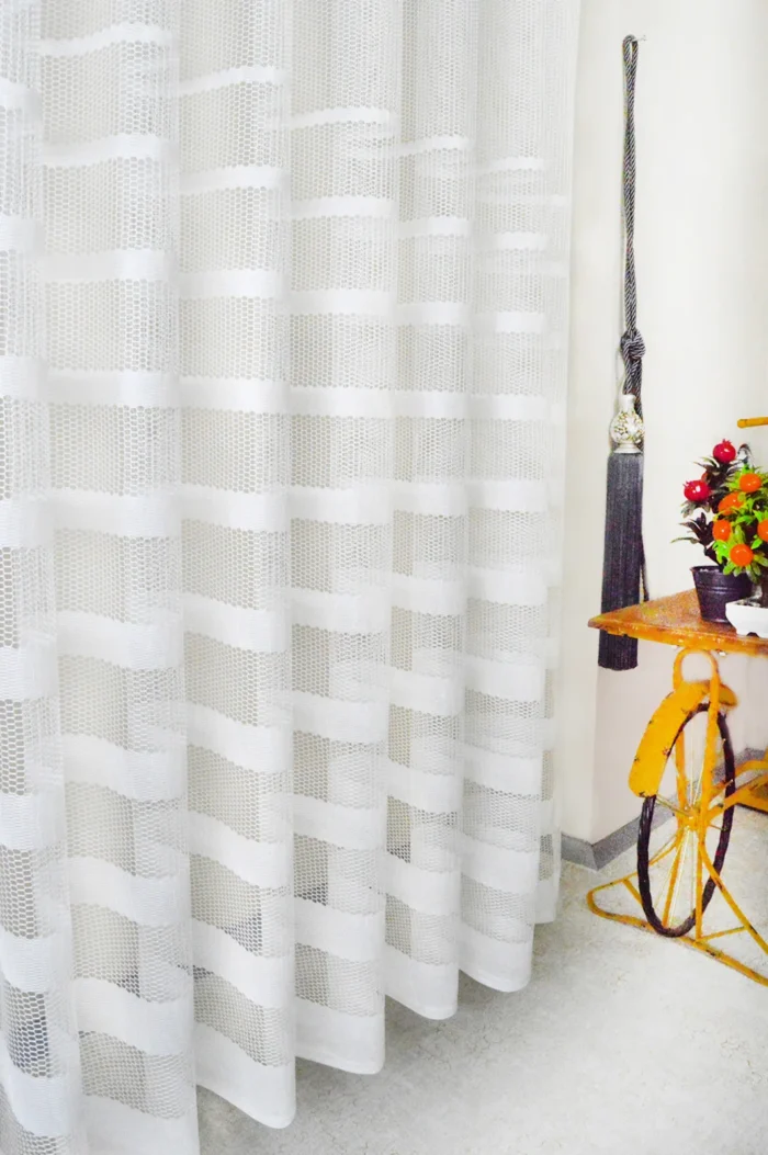 Muntazam dökümü sayesinde rüzgarda formunu bozmayan, ütü gerektirmeyen ve modern bir sportiflik sunan beyaz şeritli mutfak tül perde detayı