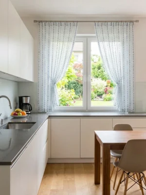 Mutfak Tasarımı: "Beyaz dolaplar ve mavi mutfak aksesuarlarıyla dekore edilmiş modern bir mutfakta, pencerelere hareket ve tarz katan ponponlu çizgili tül perde tasarımı."