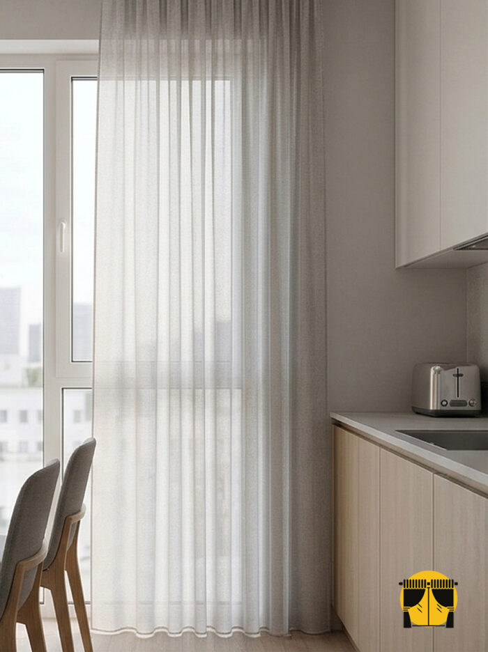 "Antrasit mutfak dolapları ve beton tezgahla dekore edilmiş endüstriyel bir mutfakta, pencerelere mimari derinlik katan gri örme tül tasarımı."