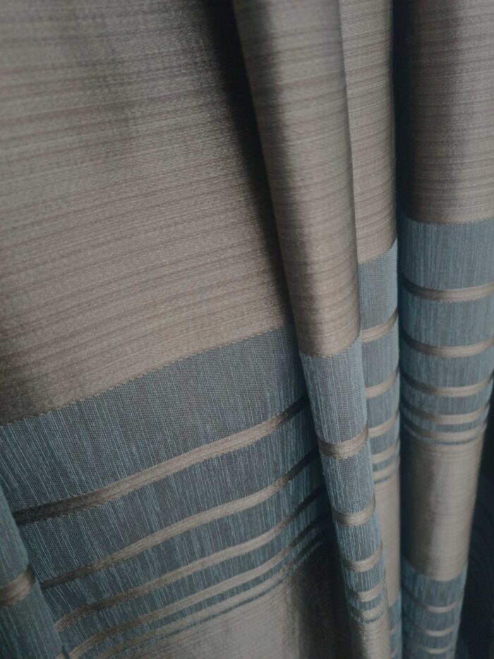 "Ekru keten tüllerle kombinlenmiş, ağır dökümü sayesinde pencerelerde maskülen bir şıklık sergileyen kahverengi-mavi fon perde uygulaması."