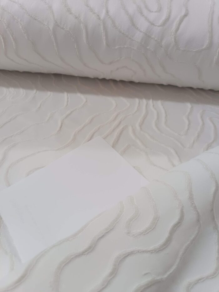 "Ekru keten tüllerle kombinlenmiş, ağır dökümü sayesinde pencerelerde heykelimsi bir şıklık sergileyen kabartmalı fon perde uygulaması."