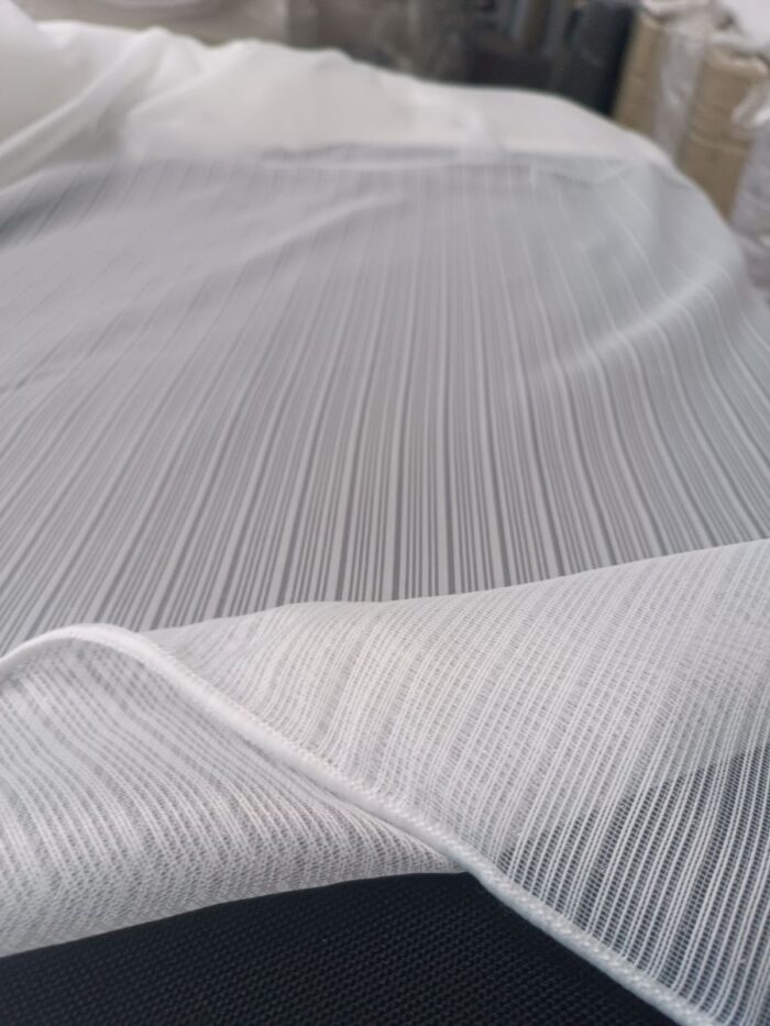 "Mat siyah metal rüstik borulara asılmış, modern panel duruşu sergileyen kaliteli Huesca ekru krem dikey çizgili tül perde modeli."
