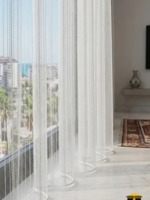 "Manorola beşik örgü desenli ekru beyaz tül perdenin kabartmalı narin dokusunun modern bir salonda yarattığı rafine, ferah ve lüks atmosfer."