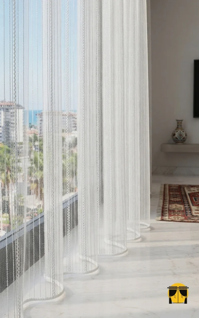 "Manorola beşik örgü desenli ekru beyaz tül perdenin kabartmalı narin dokusunun modern bir salonda yarattığı rafine, ferah ve lüks atmosfer."